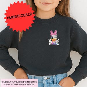 A young girl wearing a black sweater with a cartoon character embroidered on it.