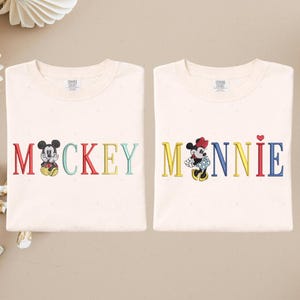 two white t-shirts with the word "MACKKEY" and the name "MANNIE" printed on them, along with illustrations of Mickey Mouse and Minnie Mouse.