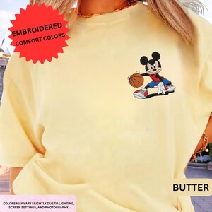 The image is a close-up of a person wearing a yellow t-shirt with a cartoon character of Mickey Mouse holding a basketball.