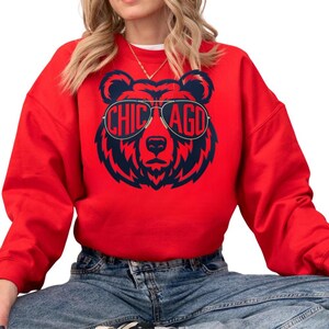 A woman wearing a red sweatshirt with a graphic of a bear wearing sunglasses and the text "CHICAGO" printed on it.