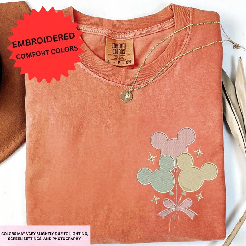 a red t-shirt with a Disney-themed design, including Mickey Mouse and other Disney characters, along with a necklace and a red starburst.