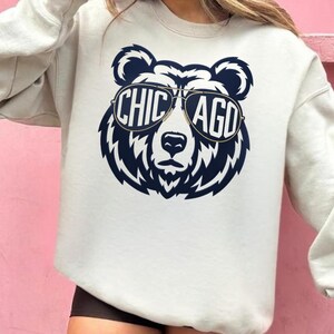 A white sweatshirt with a graphic design of a bear wearing sunglasses and the text "CHICAGO" printed on it.