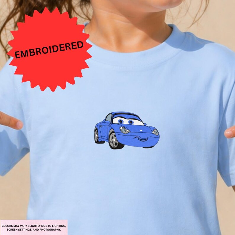 A person wearing a light blue t-shirt with a cartoon car printed on it.