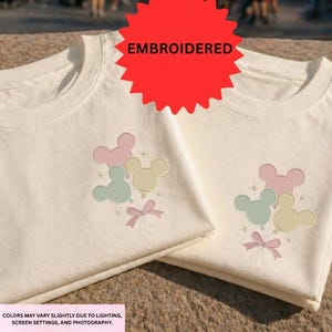 Two white t-shirts with Mickey Mouse designs and a red starburst logo, indicating that the t-shirts are embroidered.