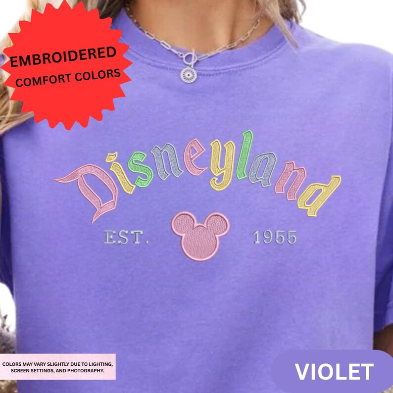 A close-up of a person wearing a purple t-shirt with the text "Disneyland EST. 1956" and a Mickey Mouse logo, along with a red starburst logo.