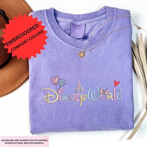 a purple t-shirt with the Disney World logo embroidered on it, along with a necklace and a hat.
