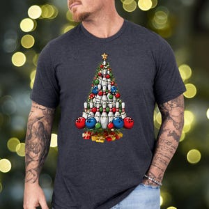 A man wearing a gray t-shirt with a Christmas tree graphic printed on it.