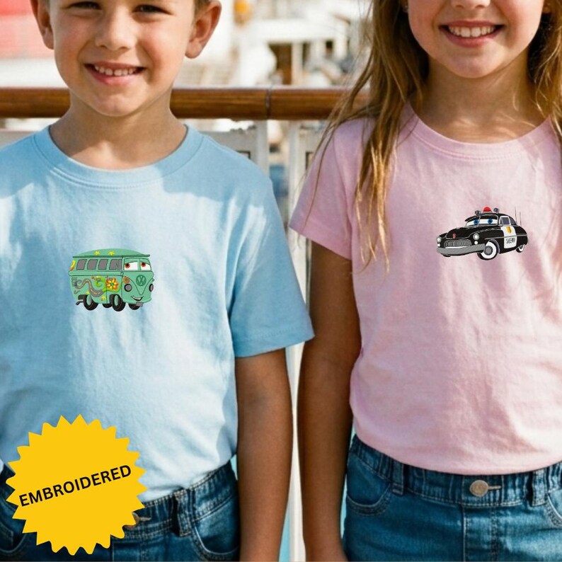 Two children wearing blue and pink t-shirts with cartoon-style vehicles printed on them, smiling and posing together.