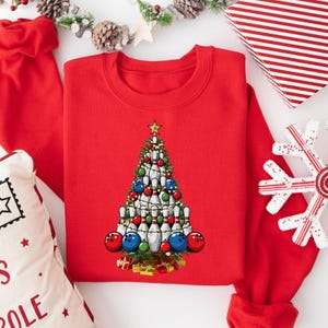 A red sweater with a Christmas tree design on it, surrounded by holiday decorations such as a snowflake, pine cones, and wrapped gifts.