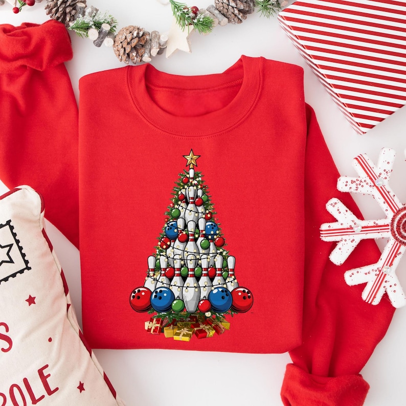 A red sweater with a Christmas tree design on it, surrounded by holiday decorations such as a snowflake, pine cones, and wrapped gifts.