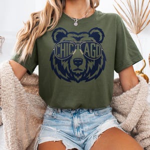A woman wearing a green t-shirt with a graphic of a bear wearing sunglasses and the text "CHICAGO" printed on it.