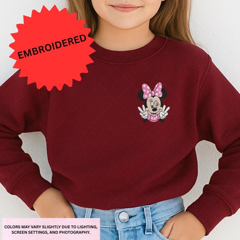 A young girl wearing a burgundy sweater with a Minnie Mouse embroidered on it.