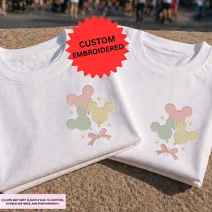 two white t-shirts with a Mickey Mouse design and a red starburst logo, indicating that the t-shirts are custom embroidered.