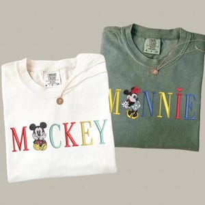 two t-shirts with the word "MICKEY" printed on them, along with images of Mickey Mouse.