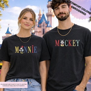 A man and a woman wearing matching t-shirts with the character Mickey Mouse printed on them, standing in front of a castle.