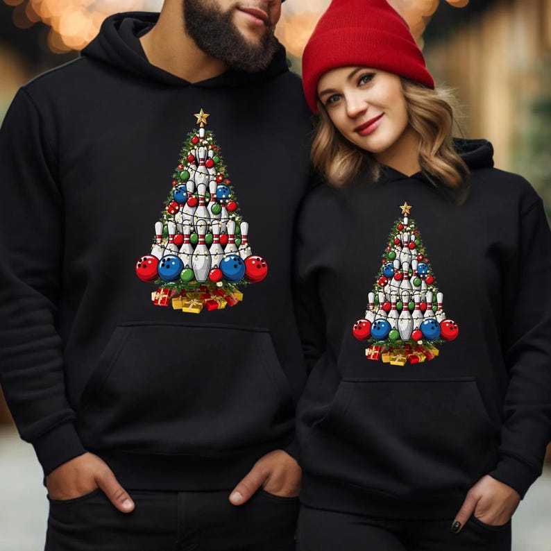A man and a woman are standing next to each other, both wearing black hooded sweatshirts with a Christmas tree design.