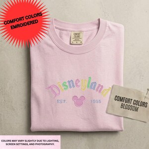 A pink t-shirt with the word "Disneyland" printed on it, along with a tag that says "Comfort Colors Embroidered" and a label that says "Conference Colors".