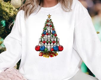 May include: White sweatshirt featuring a Christmas tree design made of bowling pins and bowling balls. The tree is decorated with red, green, and blue ornaments, a gold star, and small gift boxes at the base.