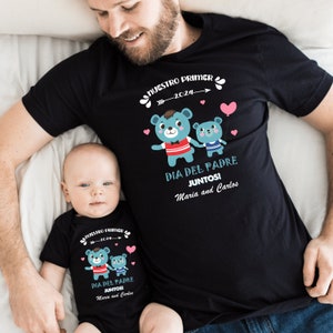 May include: A black t-shirt with a design featuring two blue teddy bears holding hands. The text "NUESTRO PRIMER -2024- DIA DEL PADRE JUNTOS! Maria and Carlos" is printed on the shirt.