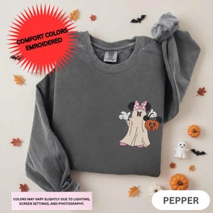 a gray sweatshirt with a Minnie Mouse design and Halloween-themed decorations, including a pumpkin and bats, all arranged on a white background.