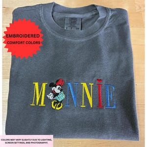 a gray t-shirt with a colorful embroidered design on it, featuring the word "Minnie" in a playful font.
