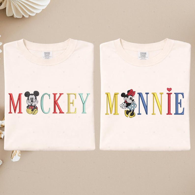 two white t-shirts with the word "MACKKEY" and the name "MANNIE" printed on them, along with illustrations of Mickey Mouse and Minnie Mouse.
