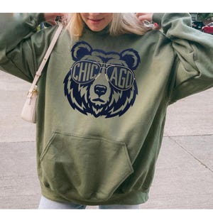 A woman wearing a green hoodie with a graphic of a bear wearing sunglasses and the text "CHICAGO" printed on it.
