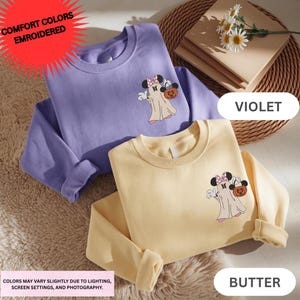 two colorful t-shirts with cartoon characters, one in purple and one in yellow, placed on a surface with a wicker basket and some flowers.