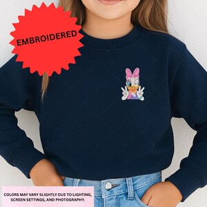 A person wearing a navy blue sweater with a cartoon character embroidered on it.