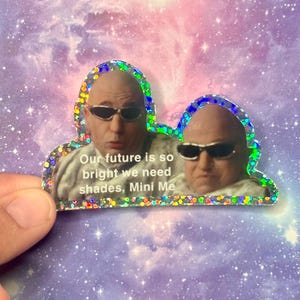 May include: A holographic sticker featuring two men wearing sunglasses with the text "Our future is so bright we need shades, Mini Me."