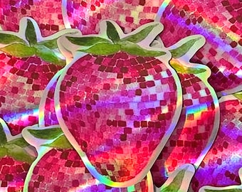 Puede incluir: Primer plano de una pila de pegatinas holográficas iridiscentes de color rosa y verde en forma de fresas. Las fresas están cubiertas de pequeños cuadrados que se asemejan a una bola de discoteca.