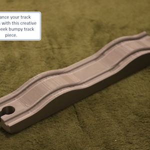 May include: A grey wooden train track piece with a bumpy surface. The track piece is designed to add a creative and sleek element to train track layouts. "Enhance your track layouts with this creative and sleek bumpy track piece."