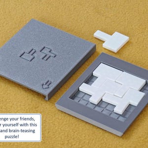 May include: A gray puzzle game with white tiles. The puzzle is in a gray frame and has a grid pattern. The tiles are arranged in a pattern that resembles a maze. The game is in a closed position, with the lid on top. The lid has two arrows pointing down and two symbols that look like a T with a square on top.