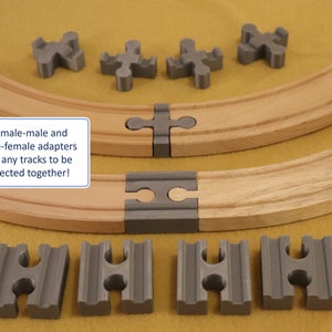 May include: Grey plastic connectors for wooden train tracks. The connectors are shaped like a cross and have two holes on each side. The text "Brio male-male and female-female adapters allow any tracks to be connected together!" is written on a white rectangle.