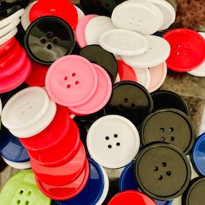 May include: A collection of various colored buttons, including red, black, white, pink, and blue. The buttons are round with either two or four holes for sewing. The image shows a variety of sizes and shades of the buttons.