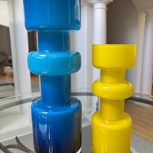 Peut inclure: Deux vases en verre, l'un bleu et l'autre jaune. Le vase bleu pr&eacute;sente un effet d&eacute;grad&eacute;, passant d'un bleu fonc&eacute; &agrave; la base &agrave; un bleu plus clair au sommet. Le vase jaune est d'une couleur vive et unie. Les deux ont un design g&eacute;om&eacute;trique unique.