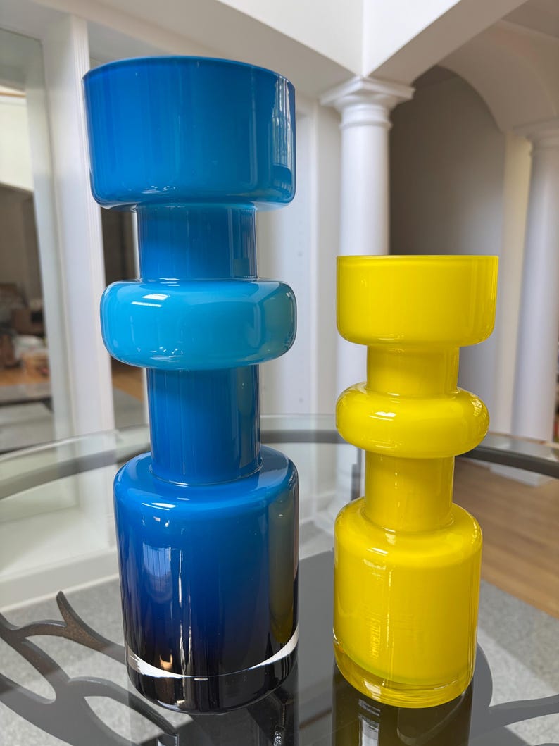 Peut inclure: Deux vases en verre, l'un bleu et l'autre jaune. Le vase bleu pr&eacute;sente un effet d&eacute;grad&eacute;, passant d'un bleu fonc&eacute; &agrave; la base &agrave; un bleu plus clair au sommet. Le vase jaune est d'une couleur vive et unie. Les deux ont un design g&eacute;om&eacute;trique unique.