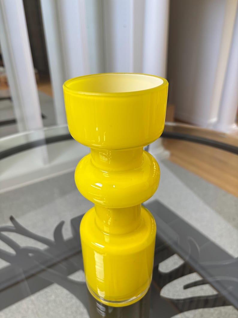 Peut inclure: Un vase en verre jaune vif avec un design empil&eacute; et bulbeux. Le vase a un large sommet ouvert et une section centrale arrondie, pos&eacute; sur une surface en verre transparent. La couleur vive et la forme unique du vase en font un &eacute;l&eacute;ment d&eacute;coratif.