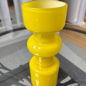 Peut inclure: Un vase en verre jaune vif avec un design unique en couches. Le vase pr&eacute;sente une base cylindrique, une section m&eacute;diane arrondie et un large sommet ouvert. Le verre a une finition brillante, refl&eacute;tant la lumi&egrave;re. C'est un objet d&eacute;coratif.