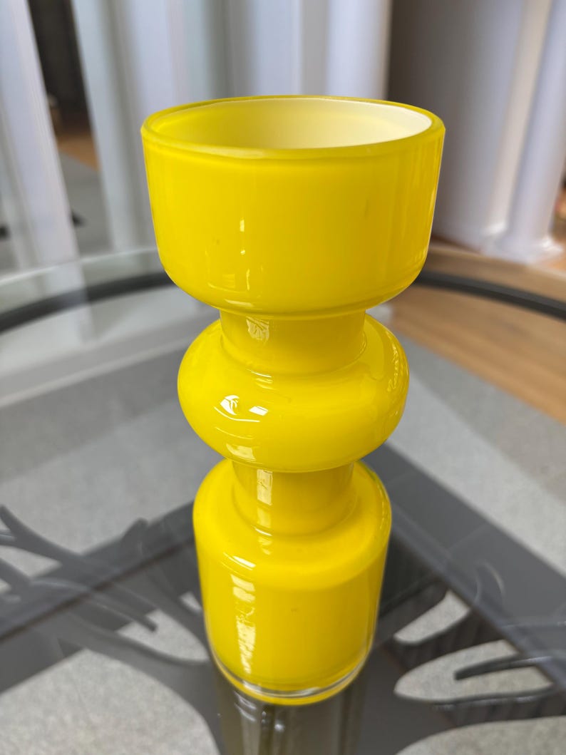 Peut inclure: Un vase en verre jaune vif avec un design unique en couches. Le vase pr&eacute;sente une base cylindrique, une section m&eacute;diane arrondie et un large sommet ouvert. Le verre a une finition brillante, refl&eacute;tant la lumi&egrave;re. C'est un objet d&eacute;coratif.