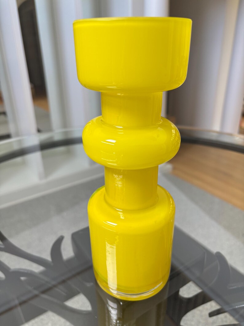Peut inclure: Un vase en verre jaune vif avec un design unique et superpos&eacute;. Le vase pr&eacute;sente une base cylindrique, une section m&eacute;diane arrondie et un sommet carr&eacute;. La finition brillante refl&egrave;te la lumi&egrave;re, soulignant la couleur vibrante. Id&eacute;al pour la d&eacute;coration int&eacute;rieure.