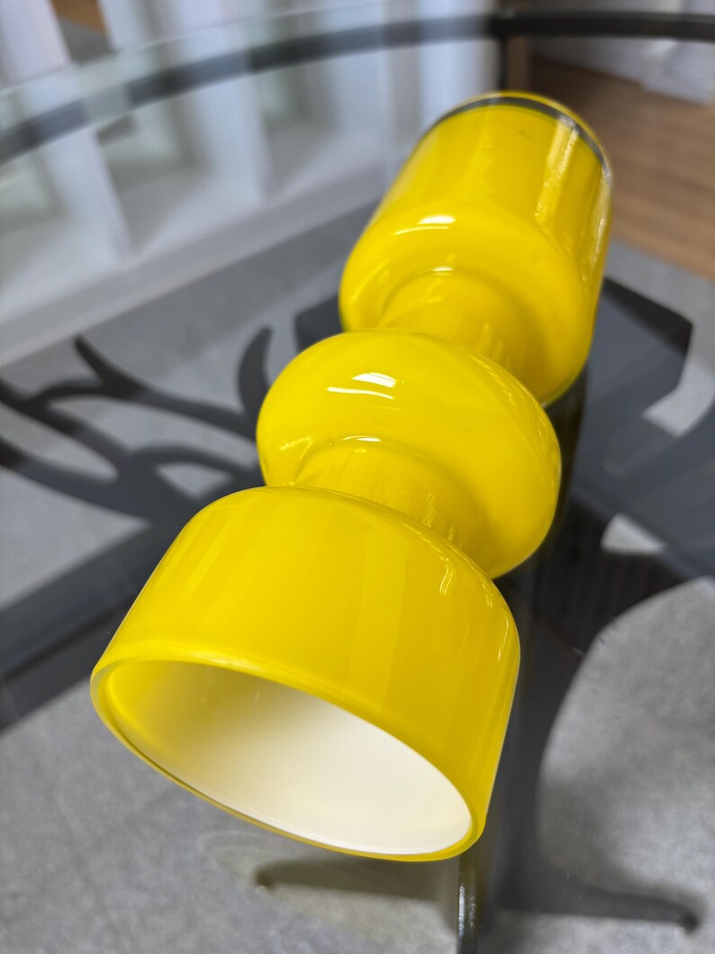 Peut inclure: Une lampe en verre jaune vif au design unique et empil&eacute;. La lampe pr&eacute;sente un dessus et un dessous cylindriques, reli&eacute;s par une section centrale arrondie. L'int&eacute;rieur de la lampe est blanc, cr&eacute;ant un contraste avec l'ext&eacute;rieur jaune vif.