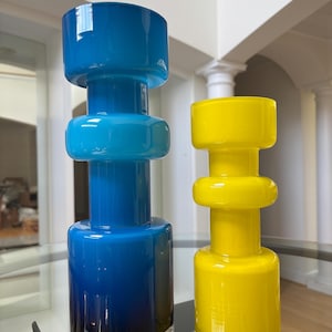 Peut inclure: Deux vases d&eacute;coratifs en verre. L'un est un d&eacute;grad&eacute; de bleu, avec une bande argent&eacute;e &agrave; la base. L'autre est jaune. Les deux ont une forme cylindrique avec un dessus et un bas arrondis, et une bande circulaire au milieu.