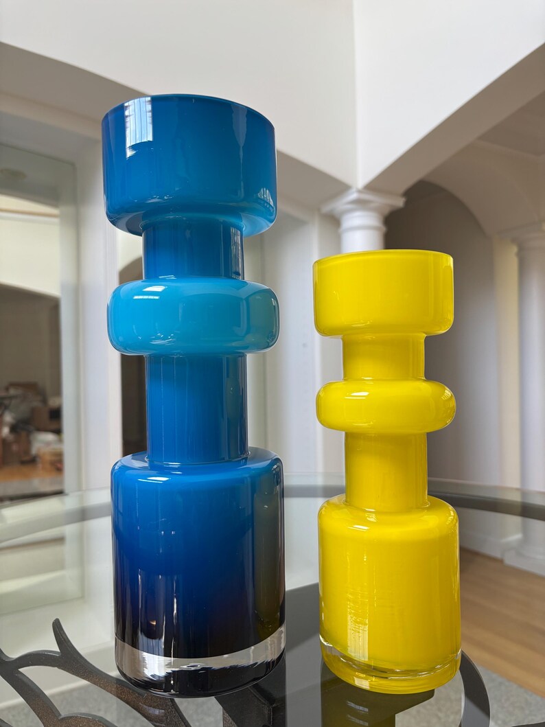 Peut inclure: Deux vases d&eacute;coratifs en verre. L'un est un d&eacute;grad&eacute; de bleu, avec une bande argent&eacute;e &agrave; la base. L'autre est jaune. Les deux ont une forme cylindrique avec un dessus et un bas arrondis, et une bande circulaire au milieu.
