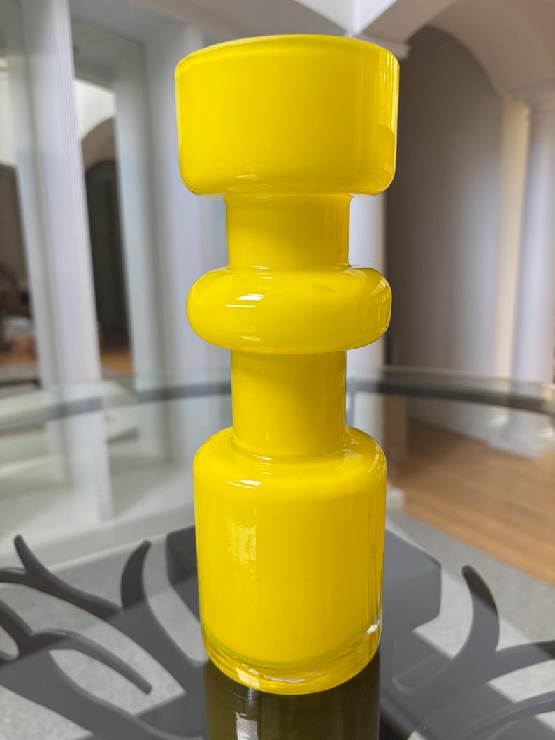 Peut inclure: Un vase en verre jaune vif avec un design unique et superpos&eacute;. Le vase a une base cylindrique, une section m&eacute;diane arrondie et un sommet plus large. La finition brillante refl&egrave;te la lumi&egrave;re, soulignant ses surfaces lisses et courbes. Cette pi&egrave;ce d&eacute;corative ajoute une touche de couleur.