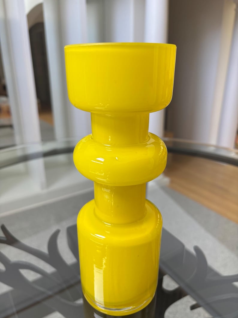 Peut inclure: Un vase en verre jaune vif avec un design empil&eacute; unique. Il pr&eacute;sente une base cylindrique, une section m&eacute;diane arrondie et un large sommet ouvert. La finition brillante refl&egrave;te la lumi&egrave;re, soulignant ses courbes lisses. Environ 25 cm de hauteur.
