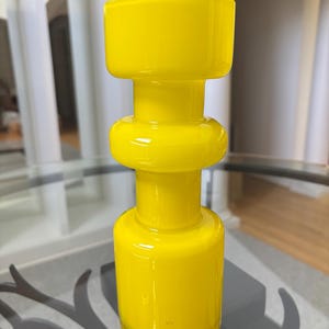 Peut inclure: Un vase en verre jaune vif avec un design unique et empil&eacute;. Le vase pr&eacute;sente une base cylindrique, une section m&eacute;diane arrondie et un sommet carr&eacute;. La finition brillante refl&egrave;te la lumi&egrave;re, soulignant la couleur vibrante et la texture lisse.