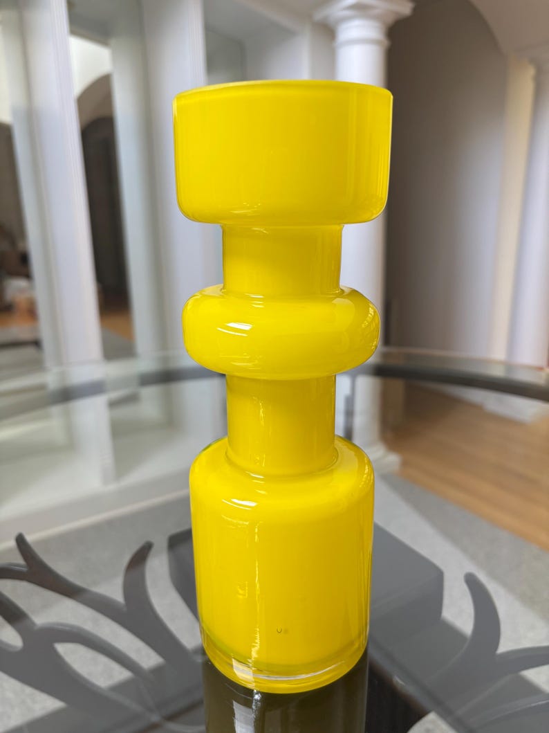 Peut inclure: Un vase en verre jaune vif avec un design unique et empil&eacute;. Le vase pr&eacute;sente une base cylindrique, une section m&eacute;diane arrondie et un sommet carr&eacute;. La finition brillante refl&egrave;te la lumi&egrave;re, soulignant la couleur vibrante et la texture lisse.