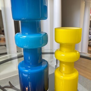 Peut inclure: Deux vases en verre de design moderne. L'un est un d&eacute;grad&eacute; de bleu, clair &agrave; fonc&eacute;, et l'autre est jaune vif. Les deux ont une base cylindrique, une section centrale arrondie et un large sommet.