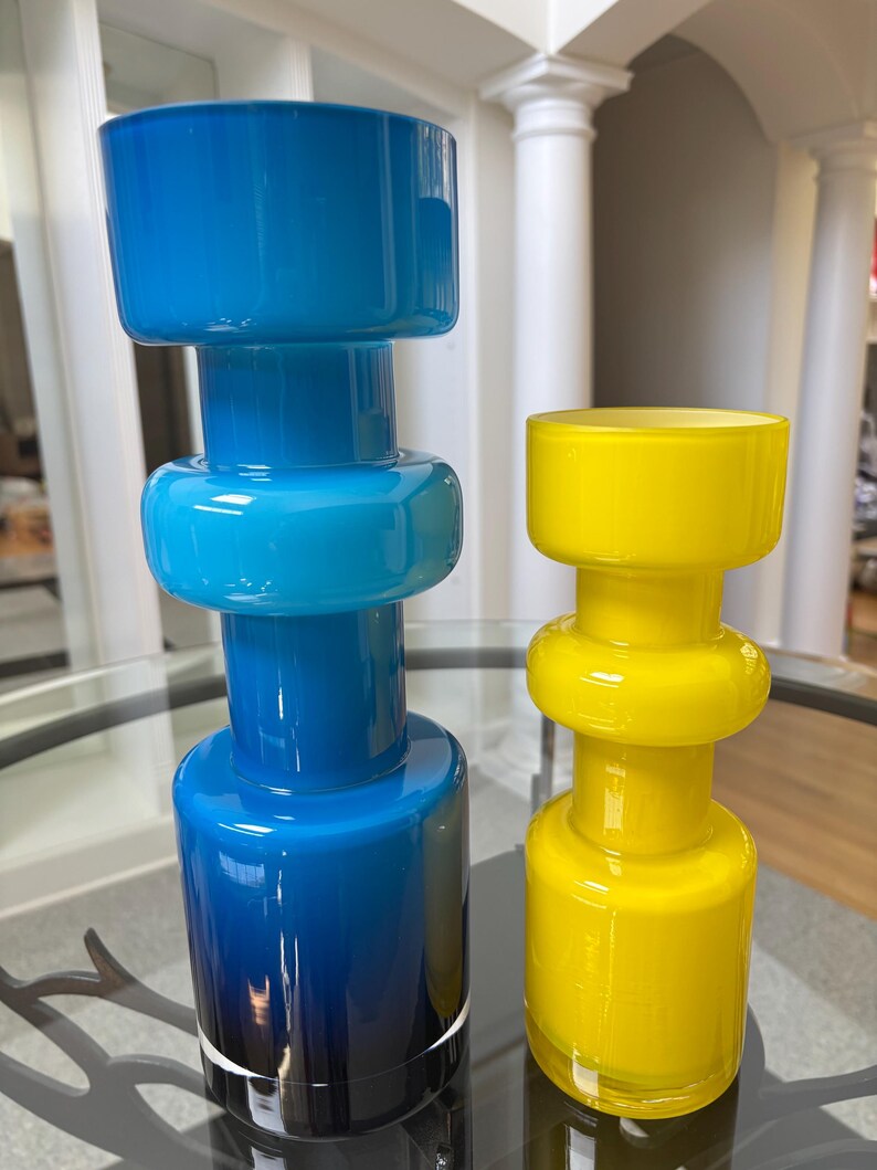 Peut inclure: Deux vases en verre de design moderne. L'un est un d&eacute;grad&eacute; de bleu, clair &agrave; fonc&eacute;, et l'autre est jaune vif. Les deux ont une base cylindrique, une section centrale arrondie et un large sommet.